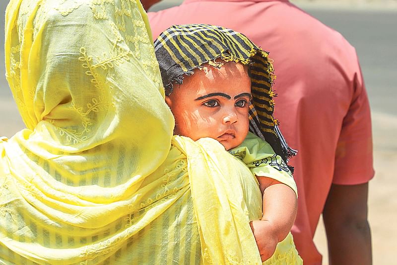 A woman covers her child's head with a handkerchief as she crosses the road in Gabtoli, Dhaka on 19 April 2024.