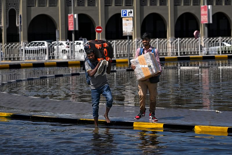 Photojournalist - Sharjah, United Arab Emirates : Men prepare to cross a flooded street following heavy rains in Sharjah on 17 April, 2024. Dubai, the Middle East's financial centre, has been paralysed by the torrential rain that caused floods across the UAE and Bahrain and left 18 dead in Oman on 14 and 15 April