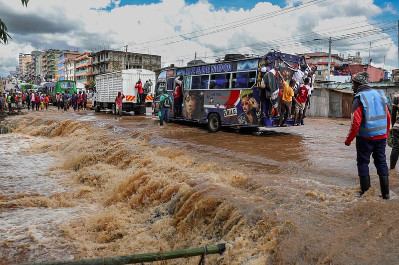 Pedestrians hang off the back of a matatu (public transport bus) to avoid having to wade across a flooded section of road after a stream burst it's banks overnight following heavy seasonal rain in the capital, Nairobi on 24 April, 2024. Storms and flash floods wreaked devastation across the Kenyan capital Nairobi on 24 April, 2024, claiming at least four lives.