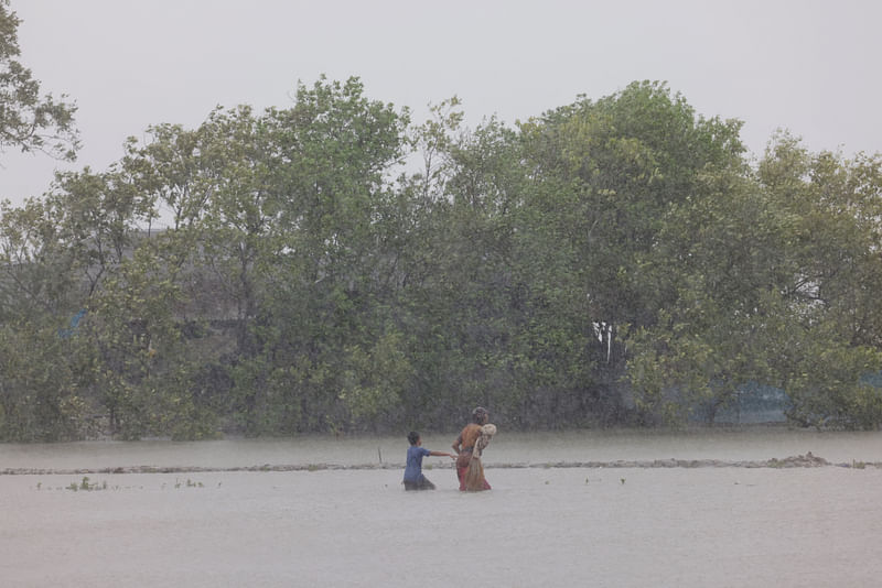 A woman and child wade through water as Cyclone Remal hits the country, in the Shyamnagar area of Satkhira, Bangladesh, on 27 May, 2024