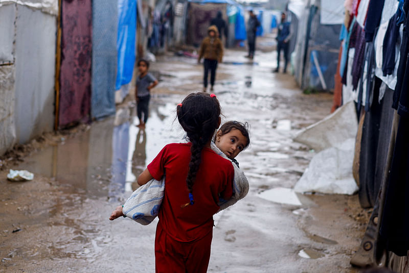 A displaced Palestinian girl holds a child as she walks at a tent camp on a rainy day, amid the ongoing conflict between Israel and Hamas, in Rafah, in the southern Gaza Strip on 6 May, 2024