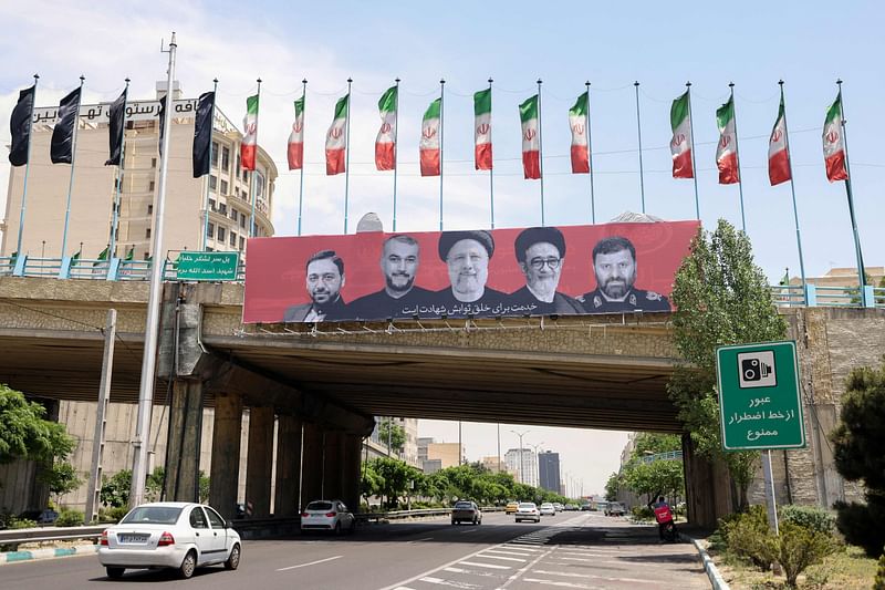 Cars drive past a billboard bearing a portrait of Iran's late president Ebrahim Raisi (C), his foreign minister Hossein Amir-Abdollahian (2nd L) and other members of his entrourage in central Tehran, on 21 May, 2024, as mourners in the northestern city of Tabriz attended a funeral procession for the president and seven others who were killed with him in a helicopter accident two days ago