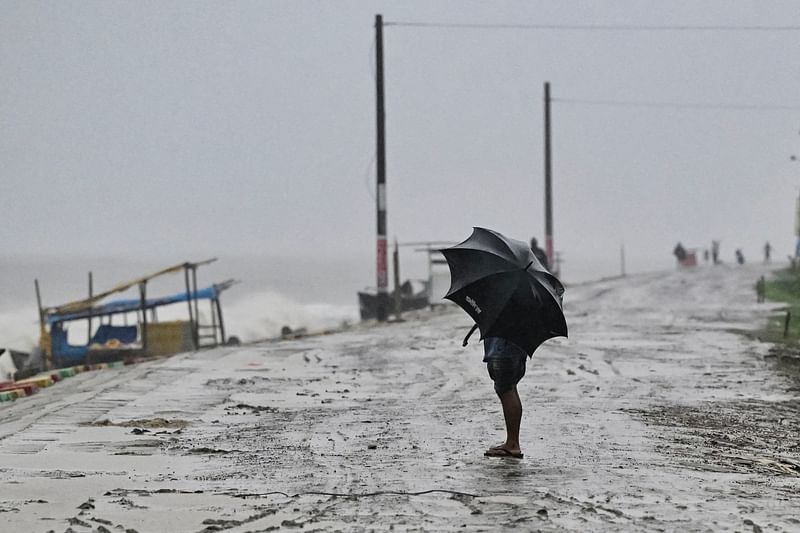 A man uses an umbrella during rainfall near a sea beach in Kuakata on 26 May 2024, ahead of cyclone Remal's landfall in Bangladesh.