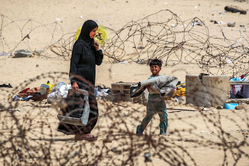 A woman and boy walk with belongings past barbed-wire fences as they flee from Rafah in the southern Gaza Strip on 11 May, 2024 amid the ongoing conflict in the Palestinian territory between Israel and Hamas.