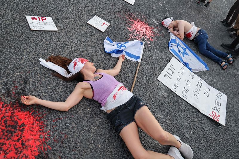 Left-wing activists covered in fake blood lie on the ground while holding national flags during an anti-government demonstration in the Israeli coastal city of Tel Aviv, on 22 June, 2024