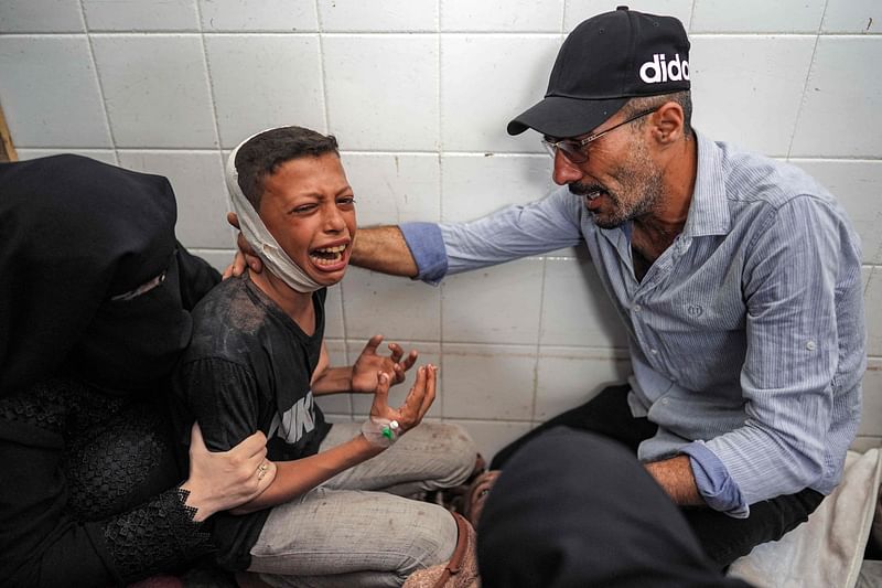 A woman and a man comfort an injured boy mourning the loss of his father who was killed in the aftermath of overnight Israeli bombardment in al-Maghazi in the central Gaza Strip, at the morgue of the Aqsa Martyrs hospital in Deir el-Balah on 25 June, 2024