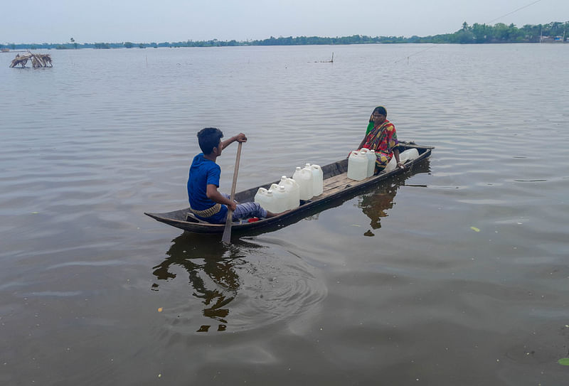 Two people on a boat after collecting drinking water in Deluti union in Paikgacha, Khulna on 31 May 2024.High tide inundates large part of the Deluti union after embankments on Bhadra River broke due to cyclone Remal, causing a crisis of drinking water.