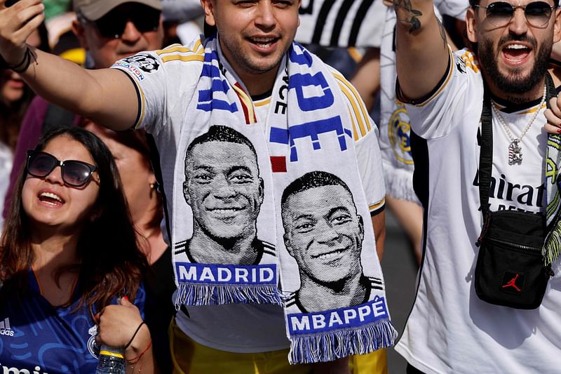 Supporters wearing football scarves depicting French footballer Kylian Mbappe cheer prior Real Madrid's celebration for winning 2024 Spanish La Liga title at Cibeles square in Madrid on 12 May, 2024