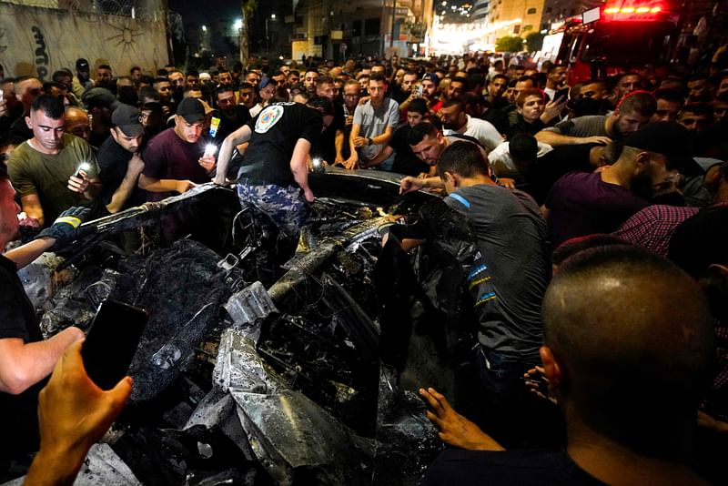 People and rescuers gather around a car targeted in an Israeli air strike that reportedly killed two Palestinians in the occupied West Bank city of Jenin on 17 August, 2024.