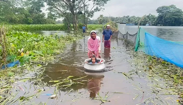 A woman carries her child in a large silver handi as the locality is under flood water