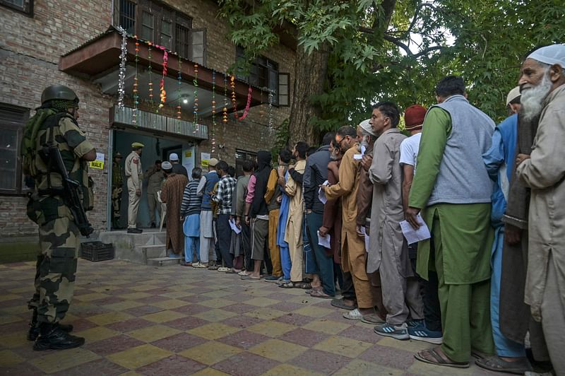 An Indian security personnel stands guard as voters queue up to cast their ballots at a polling station during the first phase of assembly elections in Pulwama, south of Srinagar on 18 September 2024.