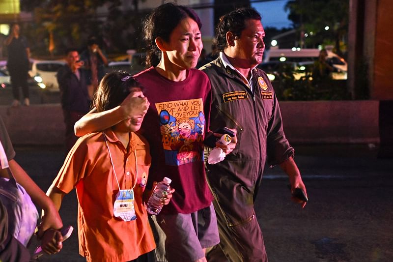 A relative (C) of a student who died in a bus fire covers the eyes of a young relative who was travelling on a separate bus on the same school trip as they walk past the burnt bus wreckage on the outskirts of Bangkok on 1 October, 2024