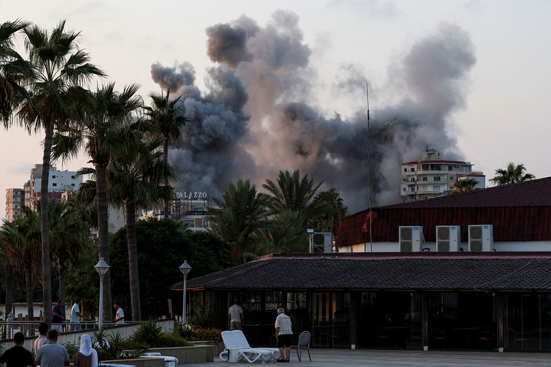 People look on, as smoke billows amid the ongoing hostilities between Hezbollah and Israeli forces, in Tyre, southern Lebanon, on 7 October 2024