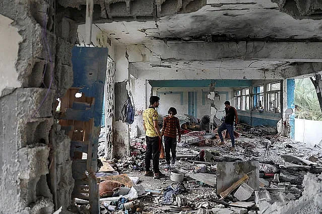 A group of people stand amid the rubble of school building following Israeli airstrike in Gaza.