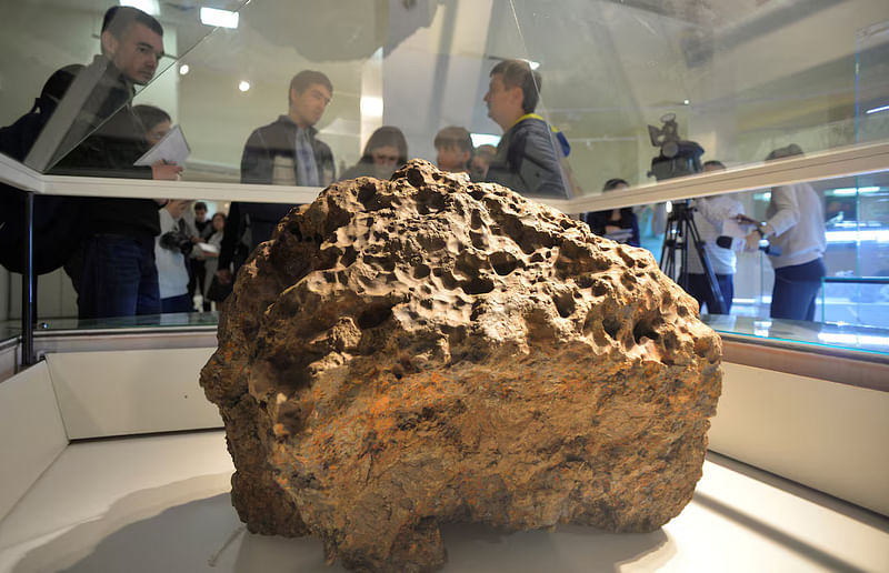 Reporters gather around a piece of a meteorite, which according to local authorities and scientists was lifted from the bottom of the Chebarkul Lake, placed on display in a local museum in Chelyabinsk, 18 October, 2013.