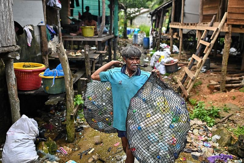 This photograph taken on September 24, 2024, shows a Moken fisherman (C) carrying bags of plastic waste to sell to Tide staff members at his fishing village on Thailand's southern island of Koh Chang in Ranong province