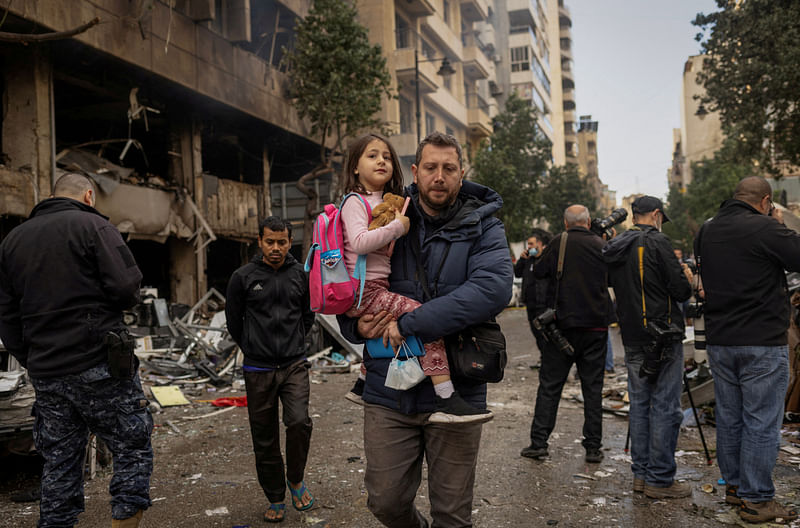 A man carries his daughter to her school as he walks past a damaged building in the aftermath of an Israeli strike, amid the ongoing hostilities between Hezbollah and Israeli forces, in Beirut’s Mar Elias street, Lebanon on 18 November 2024