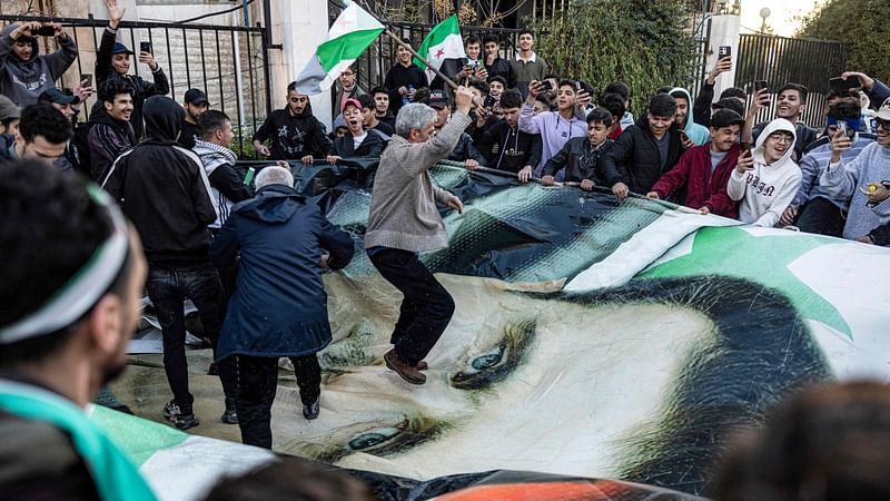 People stomp and tear apart a giant banner depicting the face of Syria's ouster president Bashar al-Assad during a rally near the Umayyad Square in central Damascus on 13 December, 2024