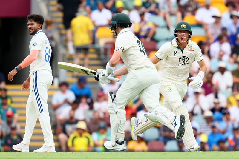 Australia's Steve Smith (C) and Marnus Labuschagne run between the wickets as Indian bowler Nitish Kumar Reddy (L) looks on during day two of the third cricket Test match between Australia and India at The Gabba in Brisbane on 15 December, 2024.