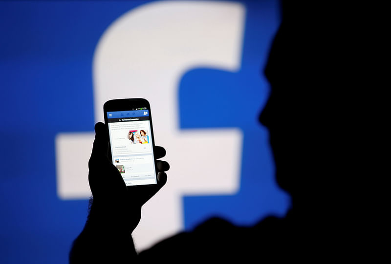 A man is silhouetted against a video screen with a Facebook logo as he poses with a smartphone in this photo illustration taken in Zenica.