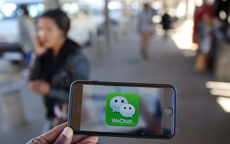 A WeChat logo is displayed on a mobile phone as a woman walks past as she talks on her mobile phone at a taxi rank in this picture illustration. Reuters file photo