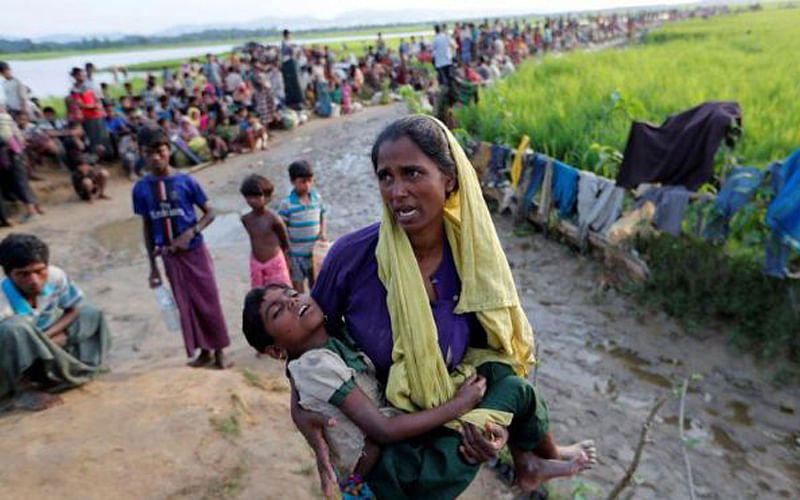 A Rohingya refugee woman who crossed the border from Myanmar a day before, carries her daughter and searches for help as they wait to receive permission from the Bangladeshi army to continue their way to the refugee camps, in Palang Khali, Bangladesh on 17 October 2017