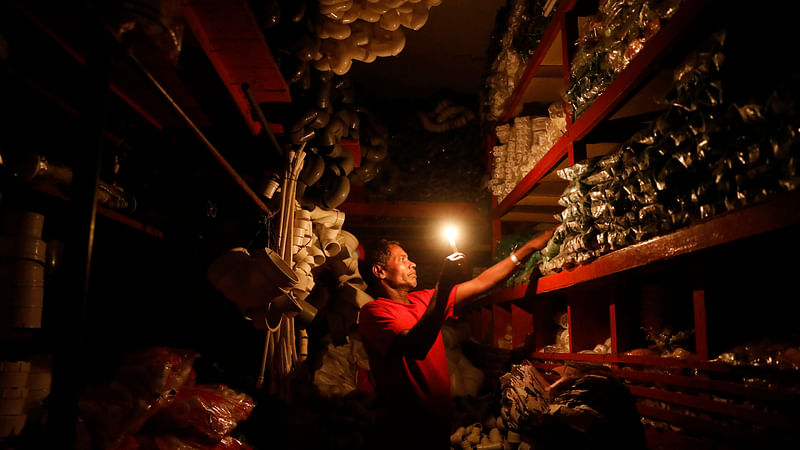 A man working in candlelight during load-shedding in Siddik Bazar area of Dhaka