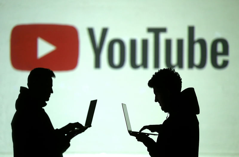 ilhouettes of mobile device users are seen next to a screen projection of Youtube logo in this picture illustration