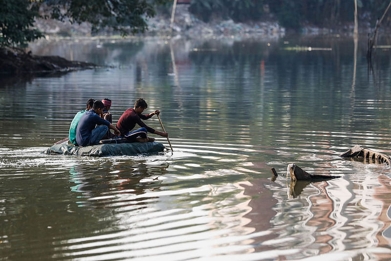 People cross Gulshan Lake in Dhaka on a raft made of bottles and cork sheets on 14 December 2019.