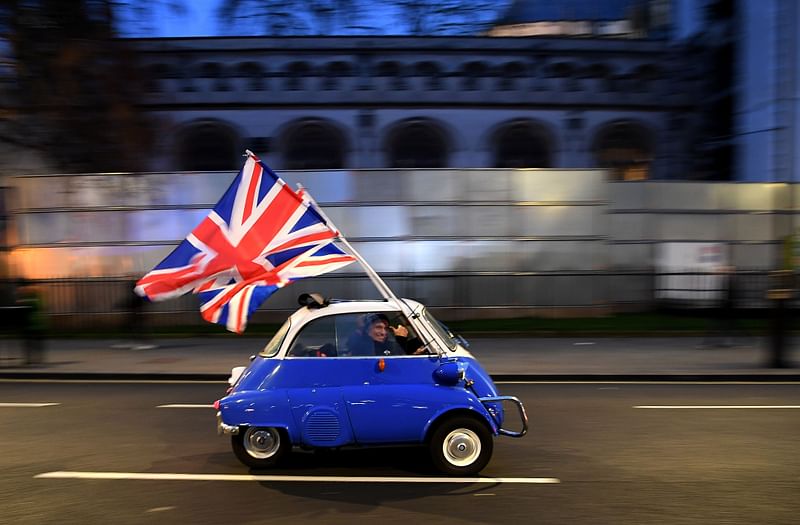 A man waves Union flags from a small car as he drives past Brexit supporters gathering in Parliament Square, in central London on 31 January 2020, the day that the UK formally leaves the European Union.