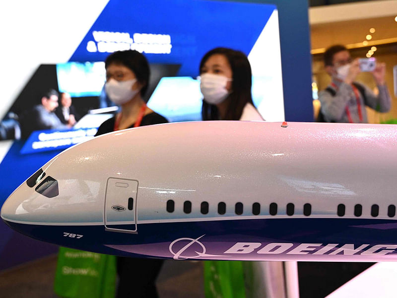 Visitors wearing protective facemasks walk past a Boeing 787 model display at the Singapore Airshow in Singapore on 12 February 2020.