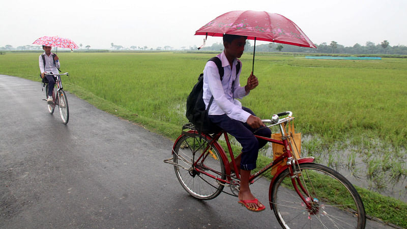 বৃষ্টির মধ্যে এক হাতে ছাতা, অন্য হাতে বাইসাইকেলের হাতল ধরে শিক্ষাপ্রতিষ্ঠানে যাচ্ছে শিক্ষার্থীরা। ১৩ জুন থেকে ২০ দিনের ছুটি শুরু হয়েছে শিক্ষাপ্রতিষ্ঠানে। ছবিটি বগুড়া সদর উপজেলার কাজী নুরুইল গ্রাম থেকে সম্প্রতি তোলা