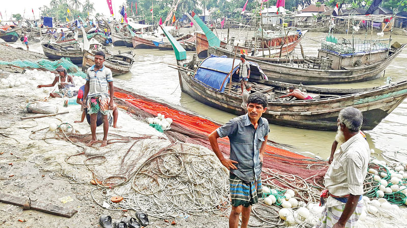 জেলেরা জাল গুছিয়ে বসে আছেন। ছবিটি ৩১ জুলাই ভোলার দৌলতখান থানার পাশের মাছঘাট থেকে তোলা l প্রথম আলো