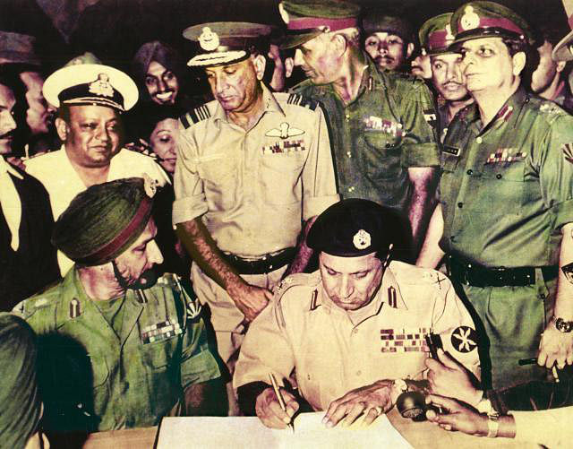 ঢাকার রেসকোর্স ময়দানে ১৯৭১ সালের ১৬ ডিসেম্বর আত্মসমর্পণের দলিলে সই করেন পাকিস্তানি বাহিনীর পূর্বাঞ্চলীয় কমান্ডের অধিনায়ক লে. জেনারেল এ এ কে নিয়াজি (ডানে)। তাঁর পাশে বসা মিত্রবাহিনীর লে. জেনারেল জগজিৎ সিং অরোরা। অরোরার ঠিক পেছনে নৌবাহিনীর সাদা ইউনিফর্ম পরা ভাইস অ্যাডমিরাল এন কৃষ্ণান l ছবি: সংগৃহীত