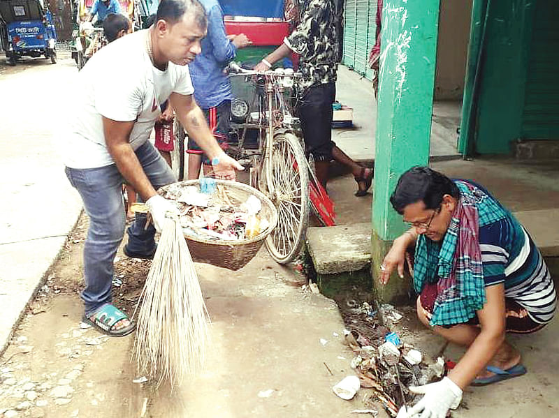 স্বেচ্ছাশ্রমে সড়কের পাশের ময়লা-আবর্জনা পরিস্কার করা হচ্ছে। শনিবার বড়লেখা পৌরসভার হাটবন্দ সড়কে।  প্রথম আলো