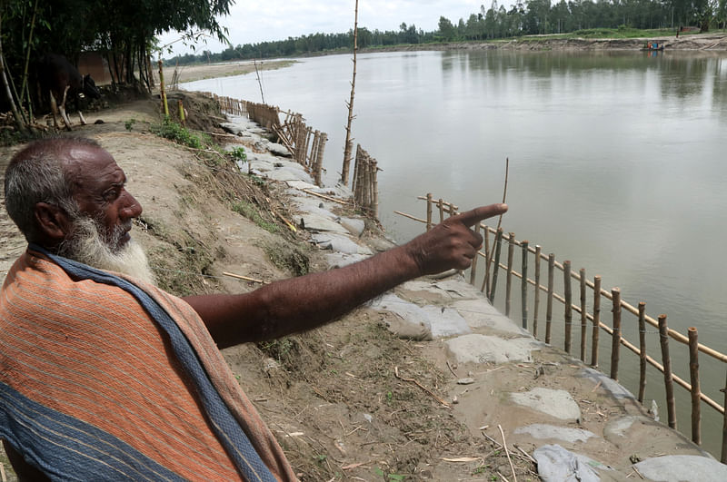 নদীর কিনারায় বসে নিজের ভেঙে যাওয়া বাড়ি দেখাচ্ছেন কৃষক আনছার আলী।