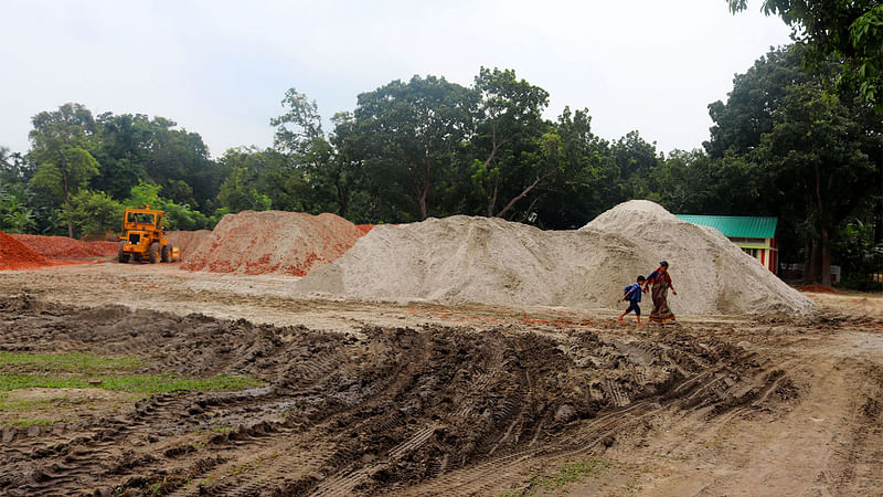 স্কুলের মাঠে সড়কের নির্মাণসামগ্রী রাখায় নাটোরের গুরুদাসপুরে হামলাইকোল সরকারি প্রাথমিক বিদ্যালয়টি আড়াল হয়েছে। ছবি: নাজমুল হাসান