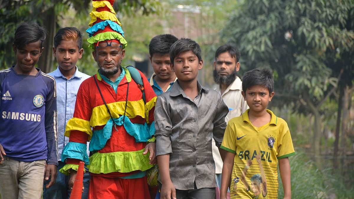 শিশুদের কাছে জোকার মামা নামে পরিচিত। শিশুদের সঙ্গে তার সখ্যও ভালো। প্রিয় জোকার মামাকে দেখে এভাবেই চানাচুর কেনার ছলে হাফিজুল ইসলামের সঙ্গে হাঁটছে শিশু–কিশোরেরা। ছবি: লেখক