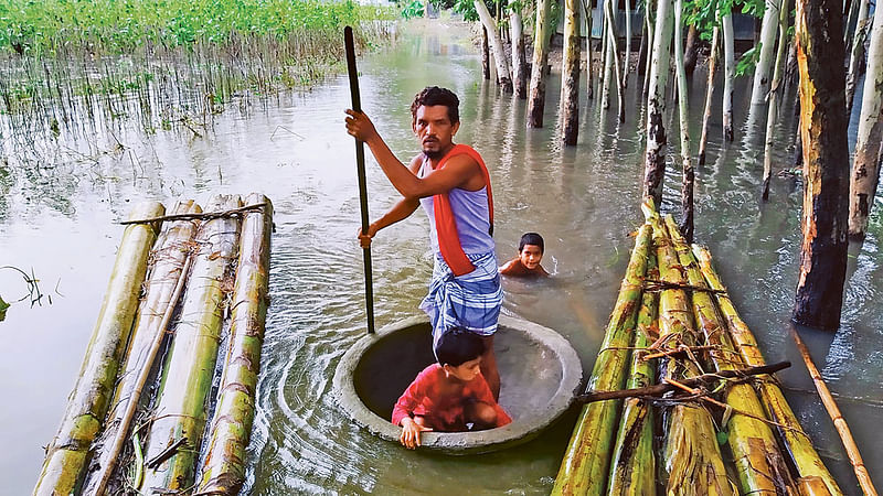 বানের পানিতে ডুবে গেছে বাড়িঘর, পথঘাট। পরিবার আশ্রয় নিয়েছে উঁচু সড়কে। বাড়ির পানি সরে গেছে। কিন্তু এখনো কাদায় পরিপূর্ণ। মেয়ে জিমকে সঙ্গে নিয়ে বাড়ির অবস্থা দেখে ফিরছেন জামাল মিয়া। ডোবা পথে হেঁটে যাওয়ার জো নেই। গরুকে খাবার দেওয়ার পাত্রে বসে পারাপার হচ্ছেন তাঁরা।  গতকাল সকালে জামালপুরের দেওয়ানগঞ্জ উপজেলার নয়াগ্রামে।  ছবি: আব্দুল আজিজ