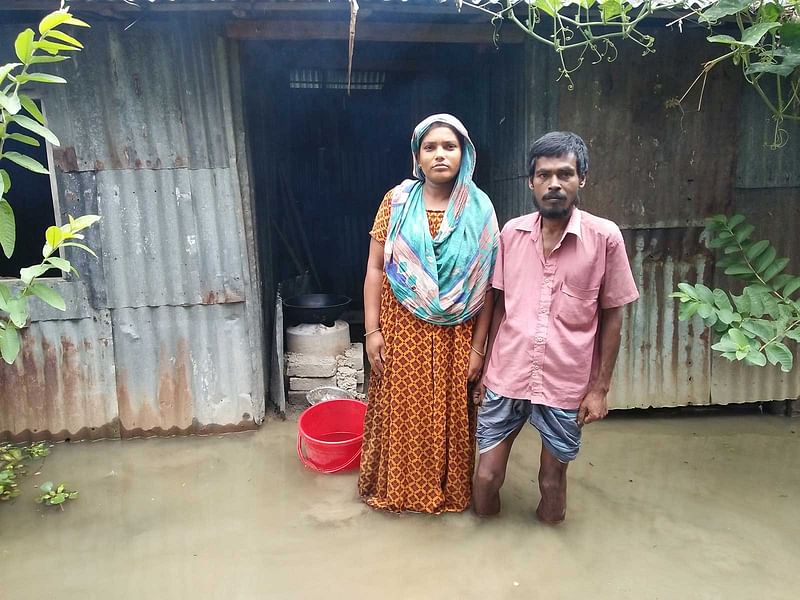 বাড়ির উঠানে পানিতে দাঁড়িয়ে আছেন দিনমজুর রোকন মিয়া ও তাঁর স্ত্রী শিল্পী আক্তার। আজ রোববার বিকেলে টাঙ্গাইলের মির্জাপুর উপজেলার মহেড়া ইউনিয়নের কড়াইল গ্রামে। ছবি: প্রথম আলো