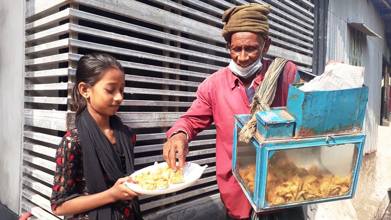 এক শিশুর কাছে শিঙাড়া বিক্রি করছেন ছোলেমান। শুক্রবার চুয়াডাঙ্গা শহরের সরদার পাড়ায়