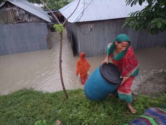 ঘরের মালপত্র উঁচু স্থানে সরিয়ে নিচ্ছেন এক নারী। বুধবার গঙ্গাচড়ার মহিপুর এলাকায়