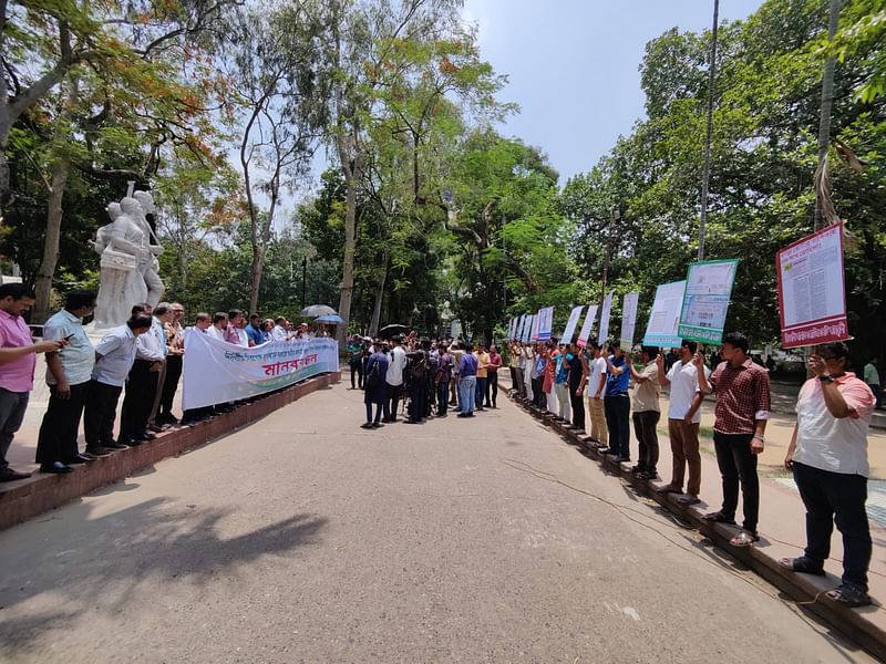 শিক্ষকদের মুখোমুখি ১০ ফুটের মতো দূরত্বে একটি করে ফেস্টুন নিয়ে দাঁড়ান ১৫ জন শিক্ষার্থী
