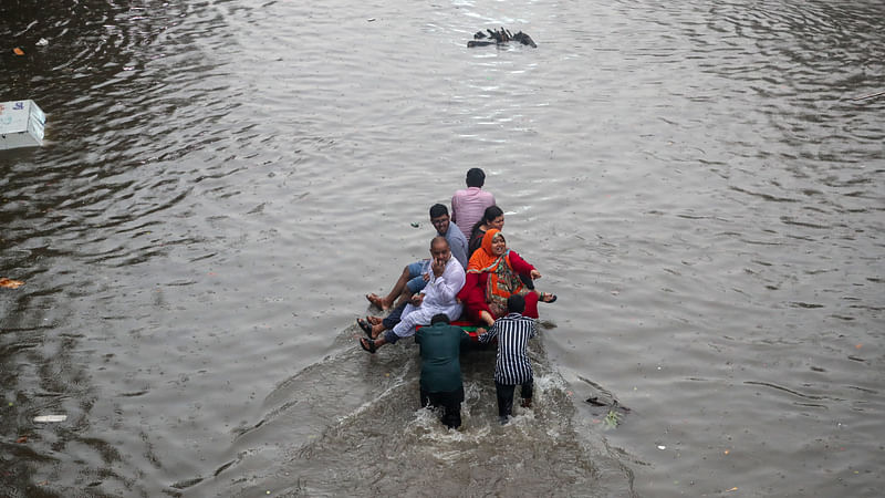 ভ্যানে উঠে ডুবে যাওয়া সড়ক পার হতে হচ্ছে। পেছন থেকে ভ্যান ঠেলে পার করছেন দুই ব্যক্তি