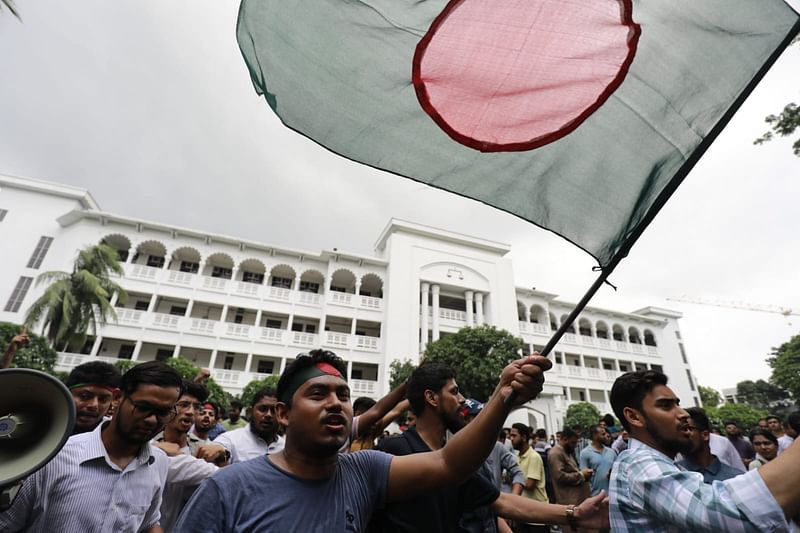 হাইকোর্ট ভবনের সামনে অবস্থানরত আন্দোলনকারীদের হাতে ছিল পতাকা। আজ শনিবার দুপুরে