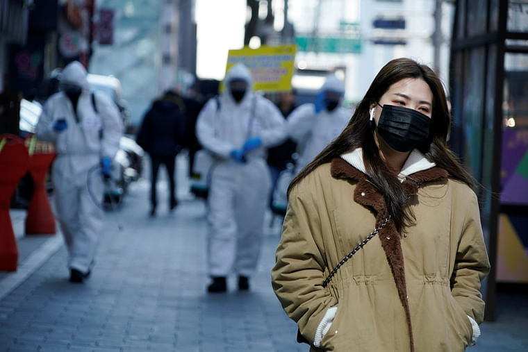 A woman wearing a mask as a preventive measure against the coronavirus walks past South Korean soldiers in protective gear sanitizing a street in Seoul, South Korea, 5 March 2020. Photo: Reuters