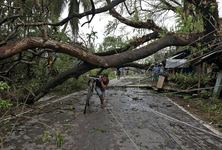 A man walks with his bicycle under an uprooted tree after Cyclone Amphan made its landfall, in South 24 Parganas district. 