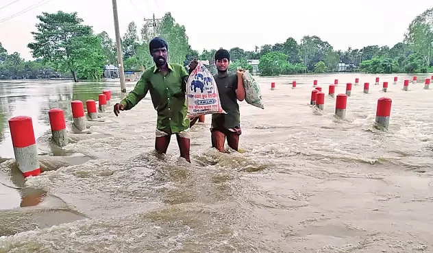 Two men carrying sacks along flooded road in Jamalpur on 30 June 2020.