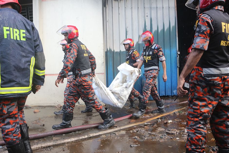 Fire service men carry remaining parts of a charred body in a bag as fire rages at a factory building of Hashem Food and Beverage Ltd. in Karnagop area of Rupganj in Narayanganj on 9 July 2021