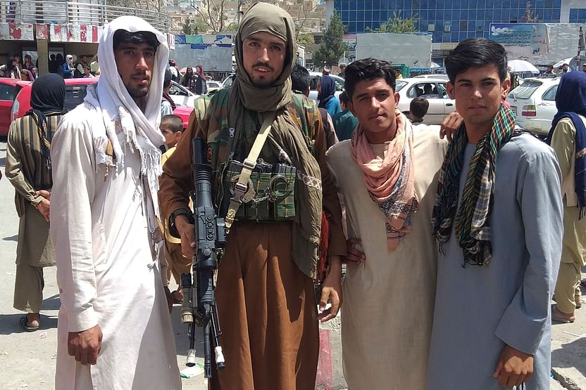 A Taliban fighter (2L) is seen with locals at Pul-e-Khumri on 11 August 2021 after Taliban captured Pul-e-Khumri, the capital of Baghlan province about 200 kms north of Kabul.